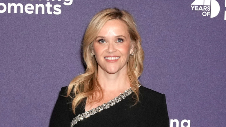 Reese Witherspoon wearing a black long-sleeved dress with a jeweled asymmetrical neckline