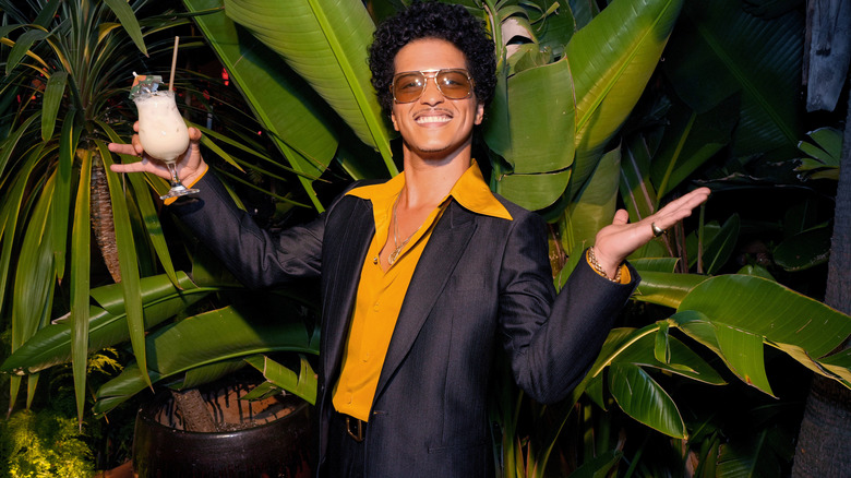 Bruno Mars holding a drink in front of a plant
