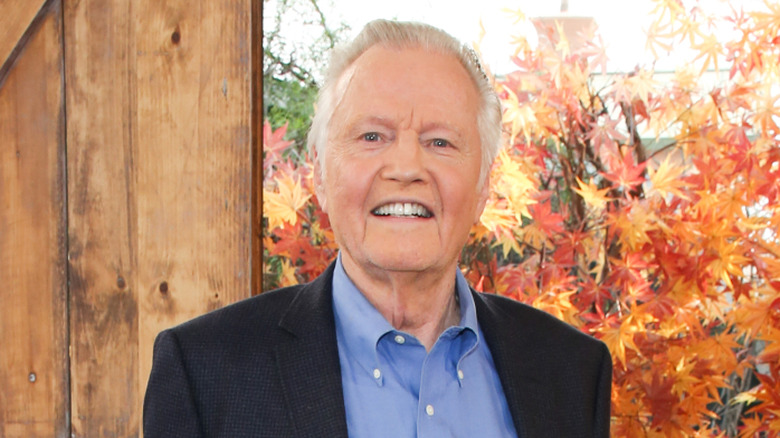 Jon Voight smiling in front of autumn leaves