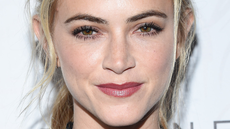 Emily Wickersham wears her hair in a ponytail and wears rosey lipstick as she smiles at an event