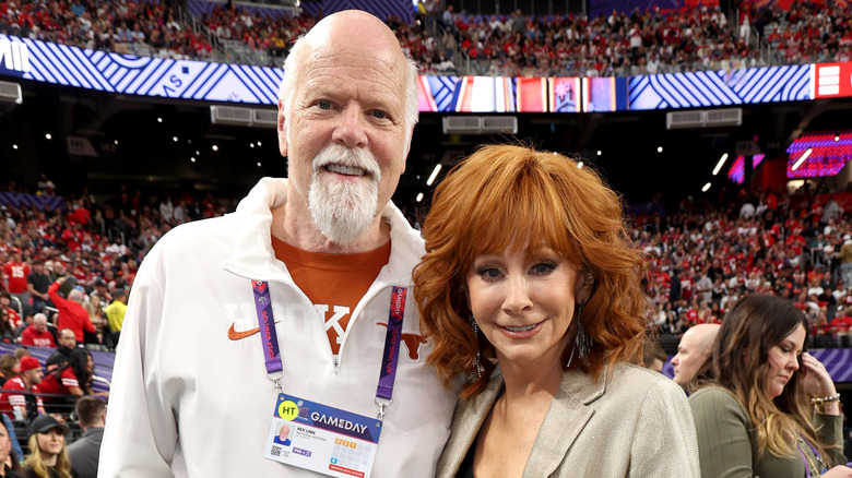 Rex Linn and Reba McEntire smiling in stadium crowd