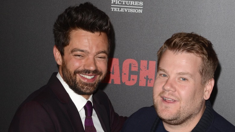 Dominic Cooper wears a burgundy tie and blazer while James Corden wears a black top on the red carpet