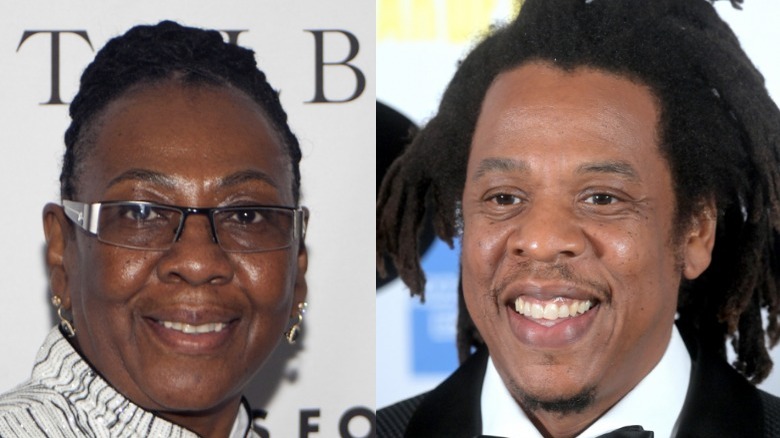 Gloria Carter smiles in a white top with black stripes, Jay-Z smiles in a suit