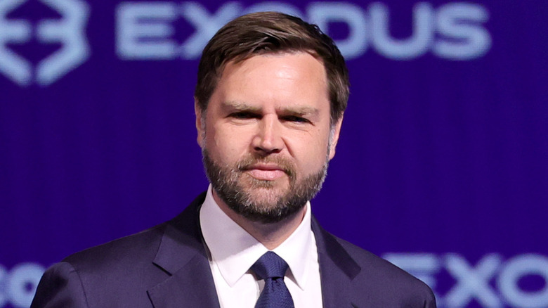JD Vance smirking while wearing a suit and blue tie.