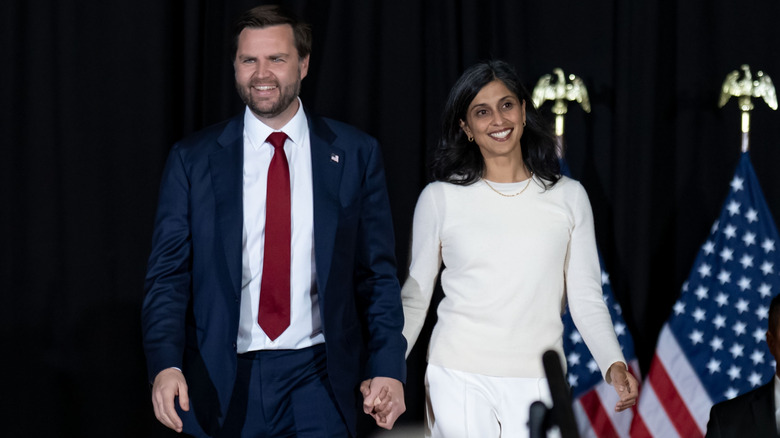 JD and Usha Vance smiling and holding hands with American flags in the background