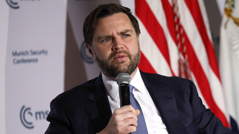 JD Vance frowning and holding a microphone