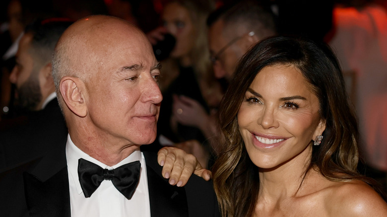 Jeff Bezos in a bowtie and suit looking at Lauren Sanchez Bezos who's wearing a silver dress at the amFar gala.