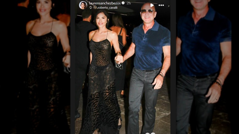 Jeff Bezos wearing a blue polo shirt and jeans while holding Lauren Sanchez's hand who's wearing a black dress.