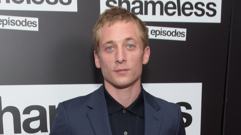 Jeremy Allen White posing in front of a black background featuring the Shameless logo