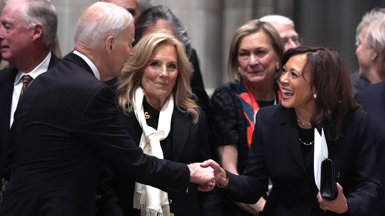 Joe Biden and Kamala Harris shake hands as Jill Biden looks directly at the camera