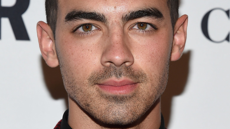 Joe Jonas poses in red and black jacket