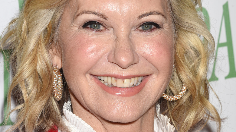 Olivia Newton-John smiles in gold hoop earrings