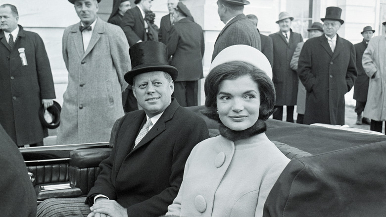 John F. Kennedy and Jackie Kennedy sit in a convertible car in 1961