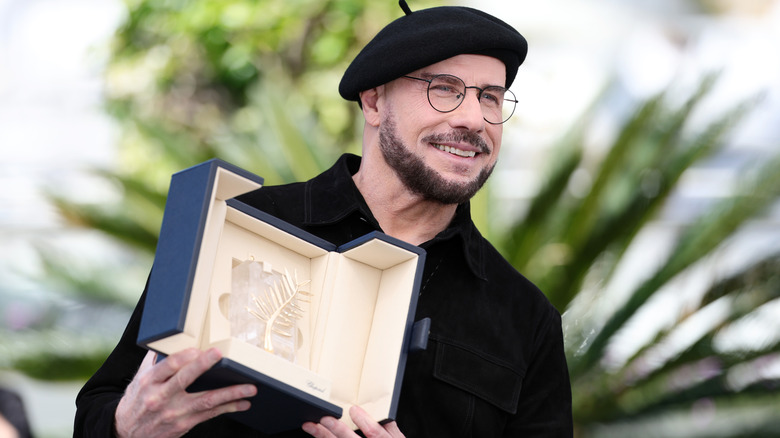 John Travolta wearing a black beret and holding his Palme d'Or Award at the Cannes Film Festival.