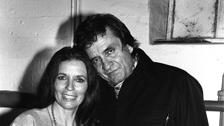 June Carter Cash and Johnny Cash posing together in front of a cement wall.