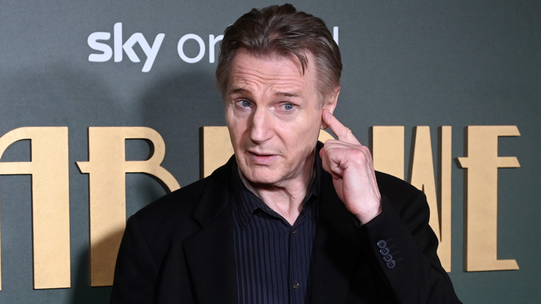 Liam Neeson holding finger to ear