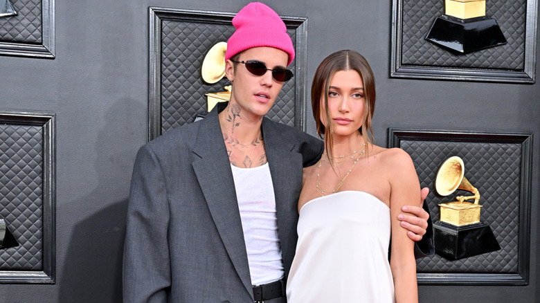 Justin Bieber wearing a pink beanie and sunglasses and posing with Hailey Bieber, who is wearing a white strapless dress, at the Grammys