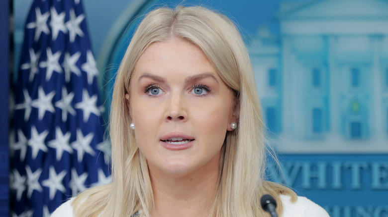 Karoline Leavitt speaking at a White House press briefing in a white outfit.