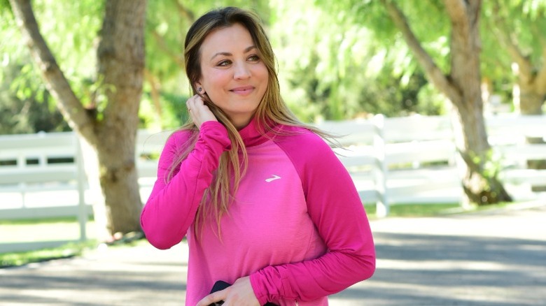 Kaley Cuoco wearing a pink long-sleeved athletic shirt and holding her phone
