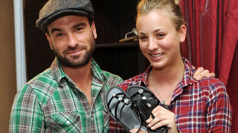 Kaley Cuoco holding up shoes beside Johnny Galecki
