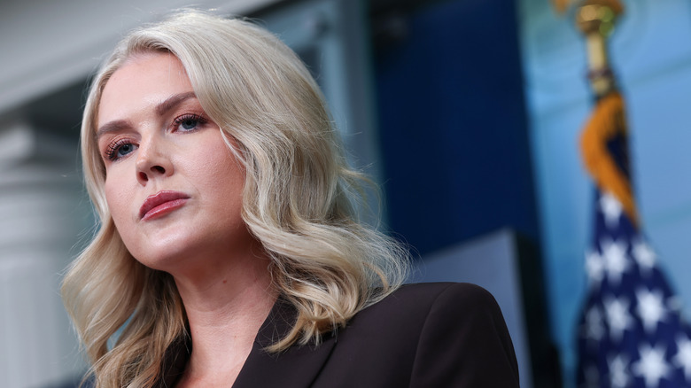 Karoline Leavitt looking grumpy in the White House press briefing room in a black blazer