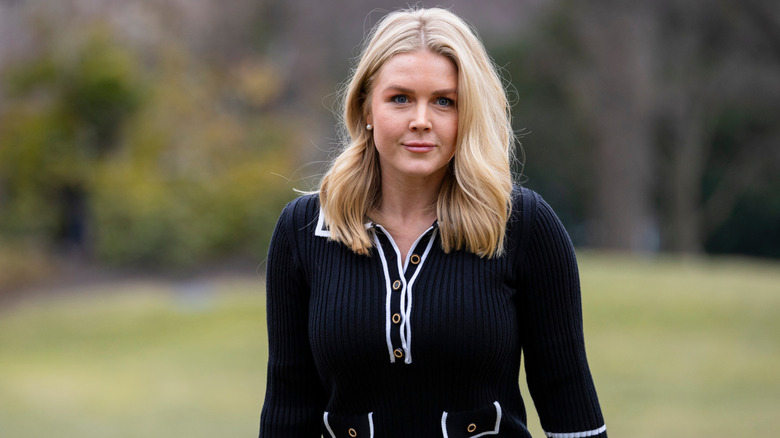 Karoline Leavitt smiling while standing in a field in a monochrome knit dress