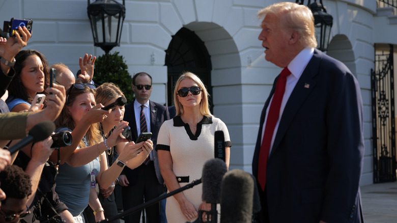 White House Press Secretary Karoline Leavitt watching as U.S. President Donald Trump talks to reporters as he departs the White House
