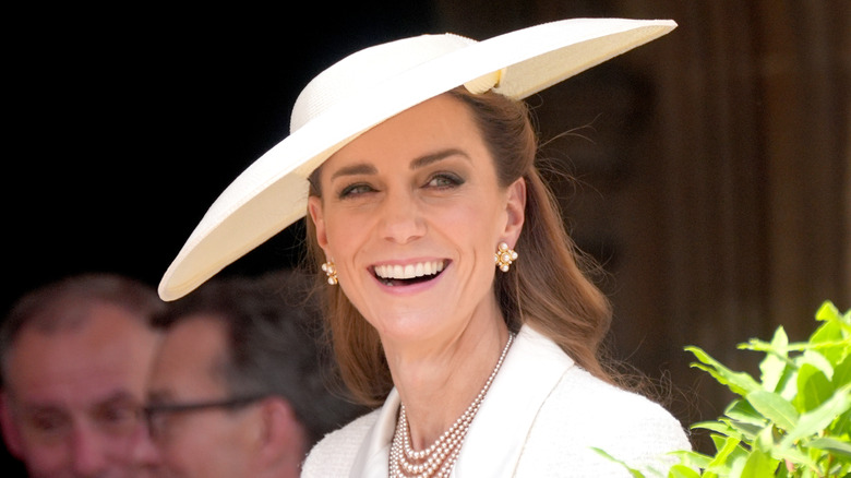 Kate Middleton smiling in white fascinator and pearls