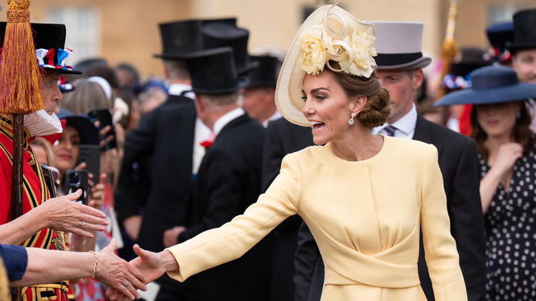 Kate Middleton wearing a yellow outfit and shaking hands with spectators