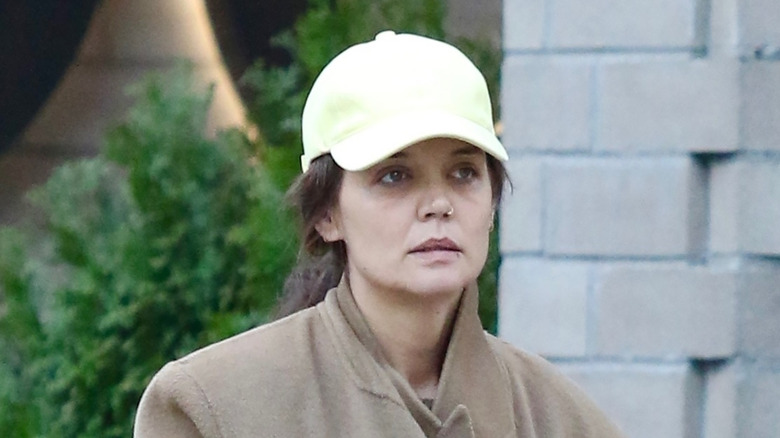 Katie Holmes standing in tan coat no makeup