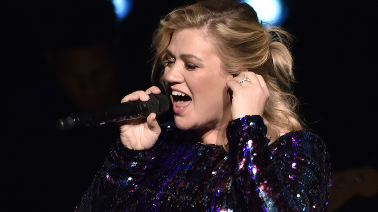 Kelly Clarkson singing and holding ear