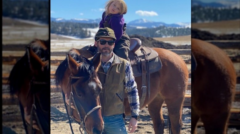 Brandon Blackstock posing in front of his daughter River Rose who's on a horse.