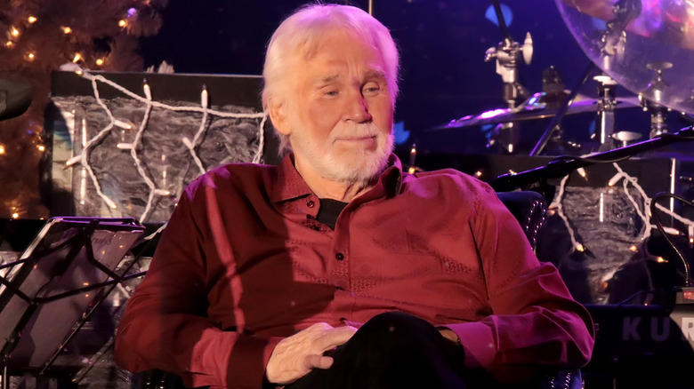Kenny Rogers seated, wearing a red shirt.