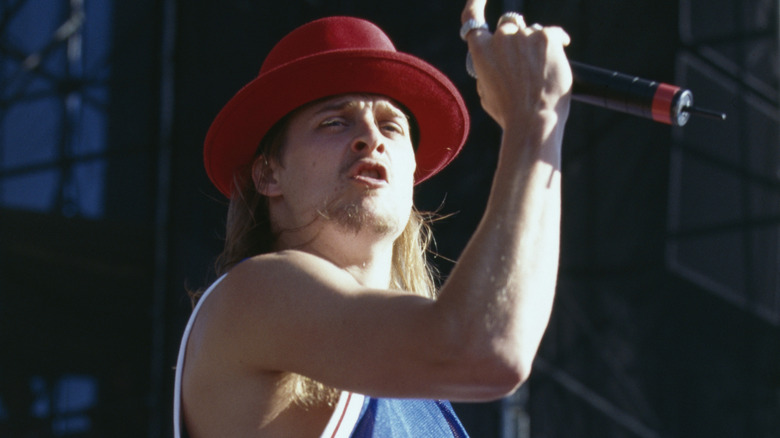 Kid Rock performing onstage wearing a red bowl hat