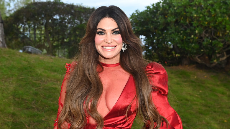 Kimberly Guilfoyle smiling while posing in a red cleavage baring dress
