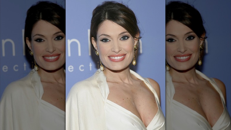 Kimberly Guilfoyle smiling in a white dress with large pearl dangle earrings.