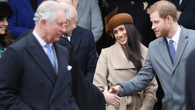 King Charles III walking in front of Meghan Markle and Prince Harry.