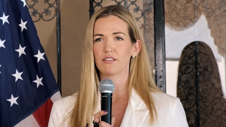 Kassidy Noem Peters holding a microphone in a cream blazer