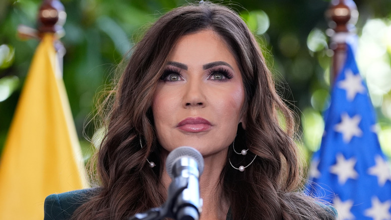 Kristi Noem standing at a podium during her 2025 trip to Ecuador