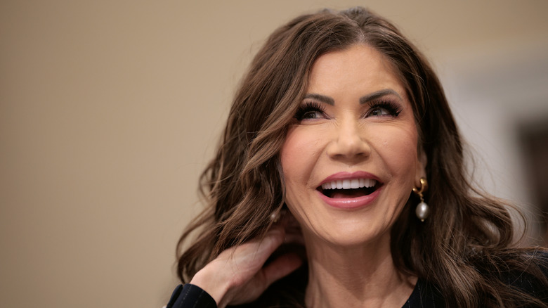 Kristi Noem smiles in May 2025 while brushing her hair away from her neck