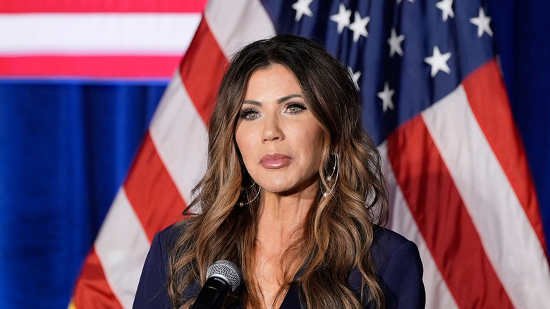 Kristi Noem in front of a microphone and an American flag
