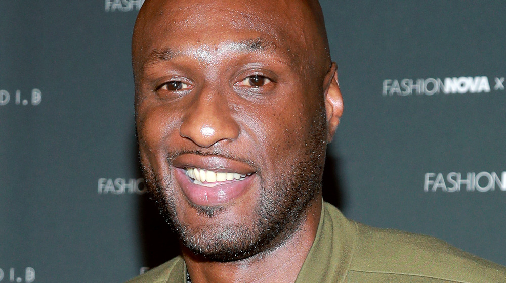 Lamar Odom smiles in an olive coat