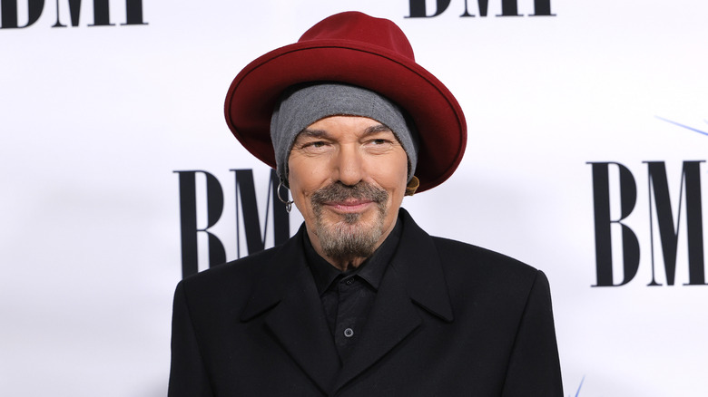 Billy Bob Thornton wearing a red hat, grey beanie, and black suit jacket and shirt
