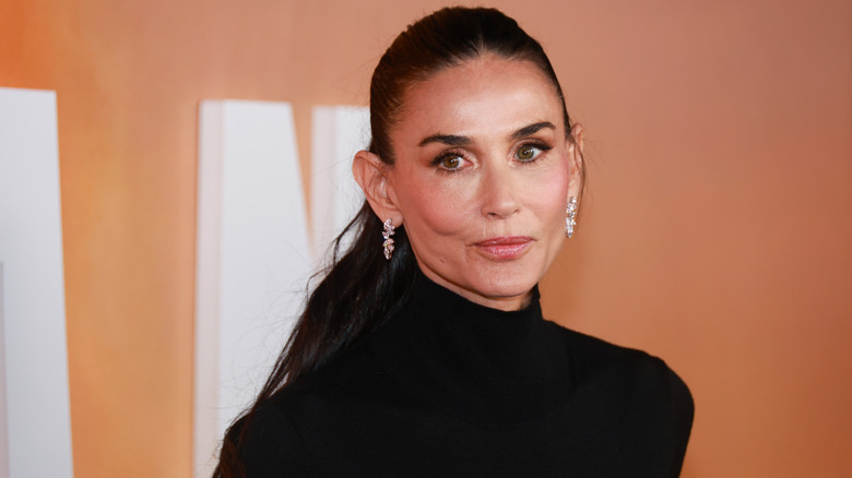 Demi Moore in a ponytail wearing a black turtleneck top and drop diamond earrings