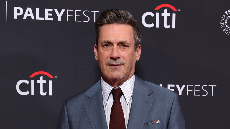 Jon Hamm wearing a grey suit and maroon tie at a red carpet event