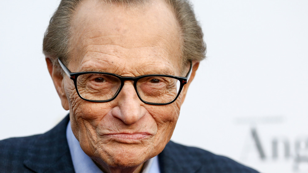 Larry King in black rimmed glasses smirks at the camera