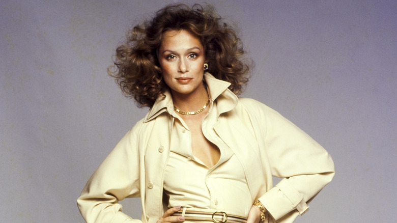 Lauren Hutton posing in cream-colored coat and shirt with her hands on her hips.