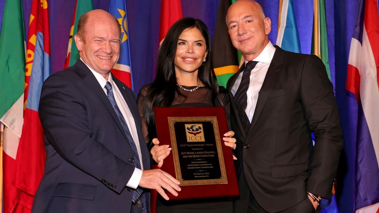Jeff Bezos and Lauren Sanchez receive an award while wearing wide smiles.