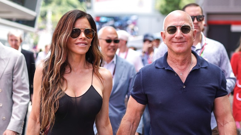 Lauren Sanchez and Jeff Bezos smile as they walk while holding hands.