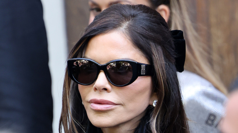 Lauren Sanchez smirking while wearing a black jacket and sunglasses during paris fashion week.